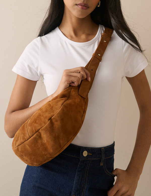 Tan suede crescent crossbody bag worn across the body
